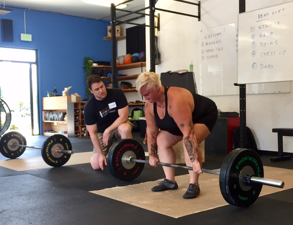 Strength coach giving a client feedback as she performs a barbell deadlift.
